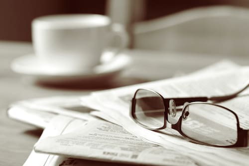 A pair of reading glasses sitting on a stack of newspapers