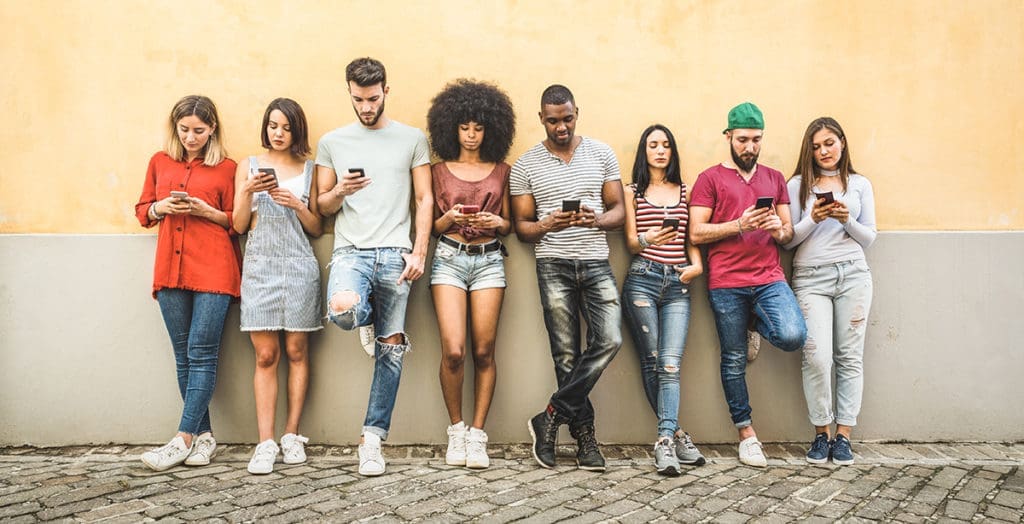 Group of young people leaning against the wall, checking their phones