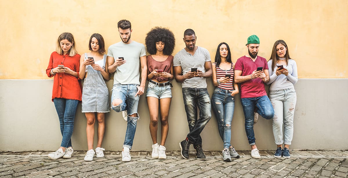 Group of young people leaning against the wall, checking their phones