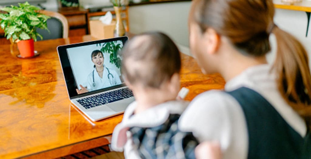 Woman holding baby, conducting a virtual visit with physician