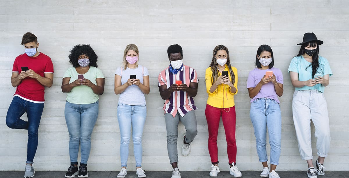 Young people leaning against a wall, wearing masks and on their phones