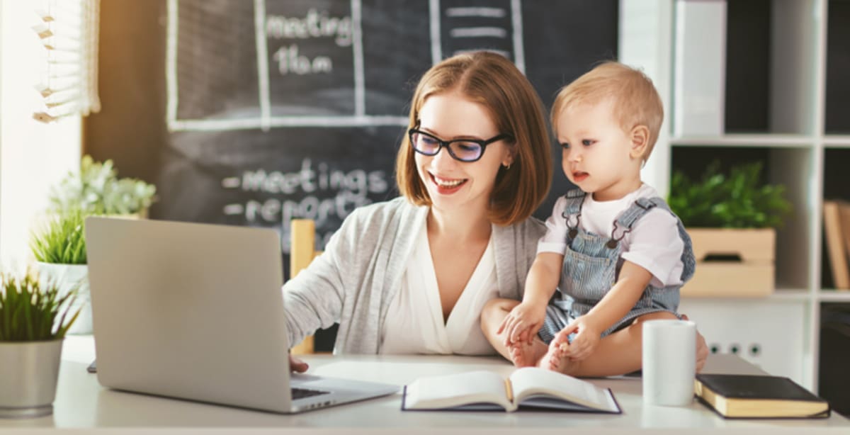 Woman on computer with baby sitting next to her