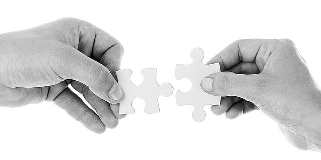 Hands fitting together two puzzle pieces