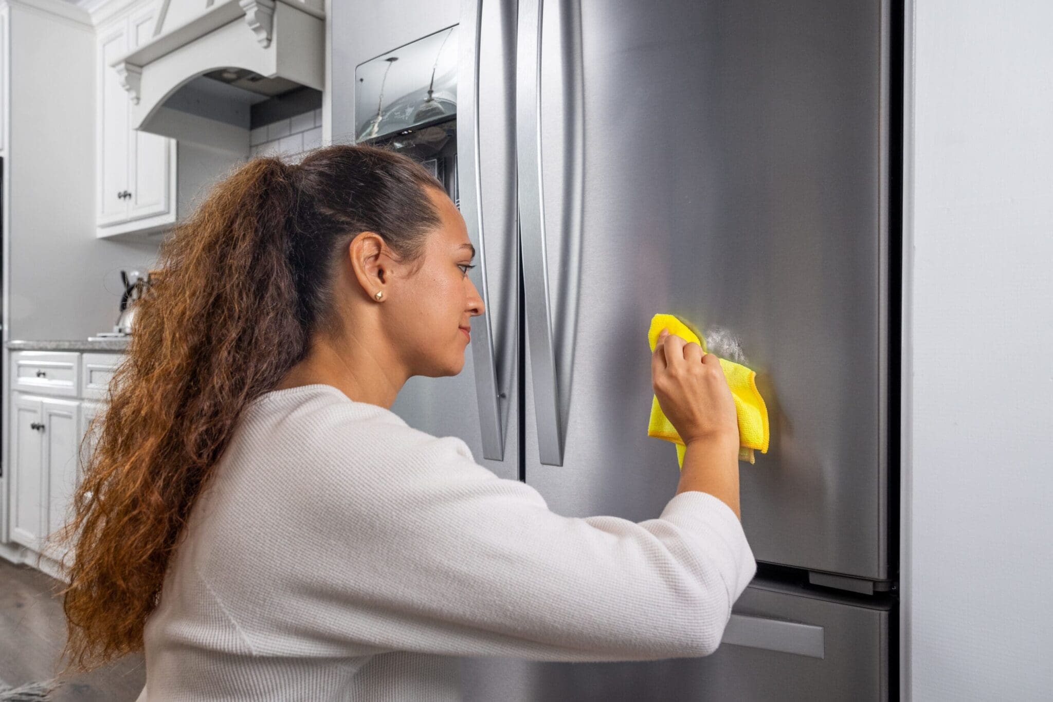 Woman removing sticker residue from fridge using Goof Off